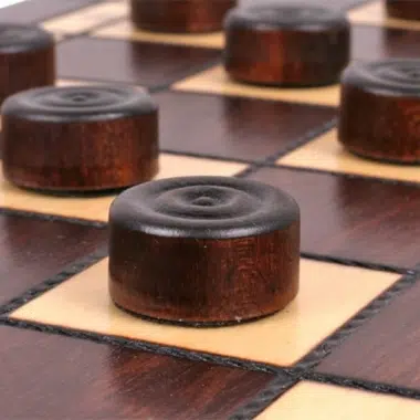 Damespiel aus Holz, dunkle Steine auf den hellen Feldern des Brettes angeordnet